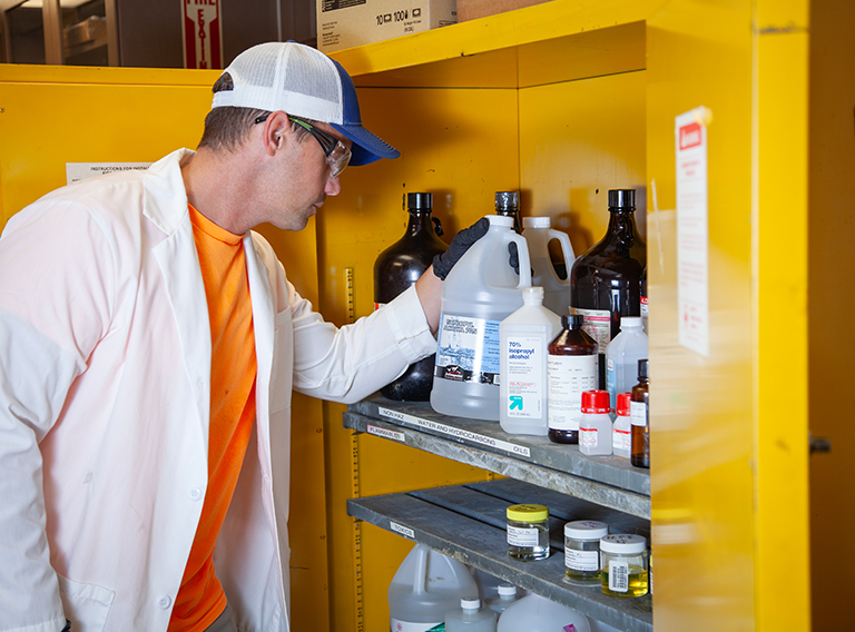 customized waste management worker wearing hat, safety glasses, and white coat working with liquids/chemicals