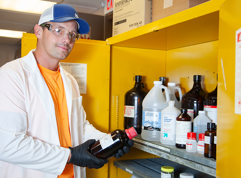 customized waste management worker wearing hat, safety glasses, and white coat working with liquids or chemicals